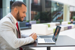 Cheerful businessman chatting via laptop. Handsome smiling young businessman using laptop computer and having video chat with friend at lunchtime. Communication concept